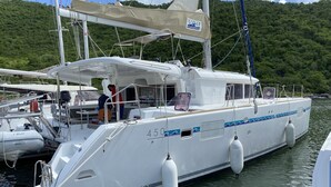 Un yate blanco amarrado en un puerto deportivo, con una colina arbolada al fondo.
