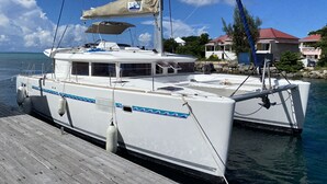 Un yate blanco amarrado a un muelle de madera con una casa al fondo.