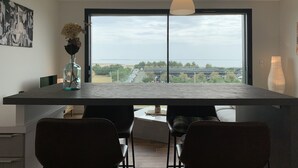 A modern kitchen with a large window, a pendant light, and a vase with flowers on the counter. - LA Petite Terrasse Lavoisier (La Rochelle)