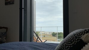 A bedroom with a bed, a small white dog, and a view through a glass door to the outside. - LA Petite Terrasse Lavoisier (La Rochelle)