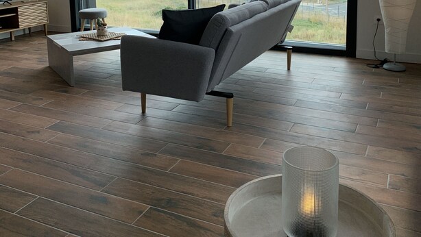 A modern living room with a grey sofa, a round coffee table, a TV on a wooden stand, and a large window with a view of a road and fields. - LA Petite Terrasse Lavoisier (La Rochelle)