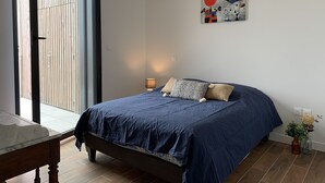 A bedroom with a bed, a nightstand, a lamp, a painting, and a view through a sliding door. - LA Petite Terrasse Lavoisier (La Rochelle)
