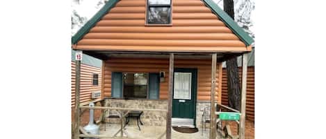 Cozy cabin with a small porch and a window above the door, set amidst a serene natural setting.