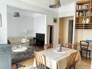 A living room with a piano, a dining table with chairs, a bookshelf, and a sofa. - Un Appartement Très Central à Deux Minutes à Pied de la Plage (Menton)