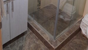 Un baño con cabina de ducha de vidrio, un lavamanos blanco y piso de baldosas de mármol.