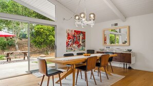 A dining area with a wooden table, chairs, a chandelier, a painting, and a mirror.