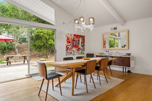 A dining area with a wooden table, chairs, a chandelier, a painting, and a mirror.