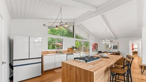 A modern kitchen with white cabinetry, a wooden island, and a large window overlooking greenery.