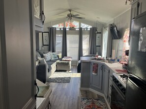 A narrow kitchen with a dining area, a ceiling fan, a refrigerator, and a stove. - Delightful, Serene Tiny Home- Casa Villa (Johnstown)