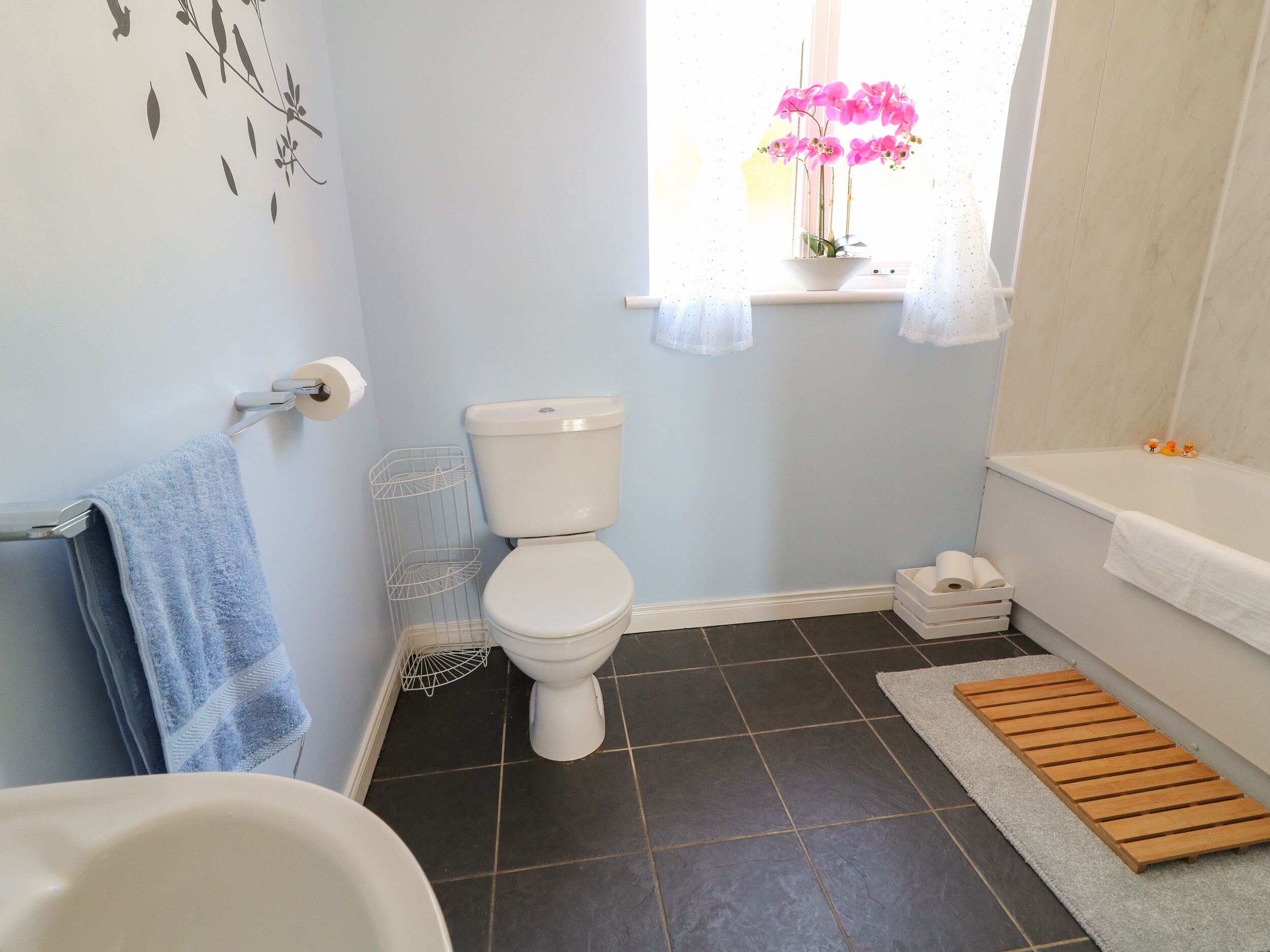 A bathroom with a toilet, a sink, a bathtub, a window with a flower, and a towel rack.