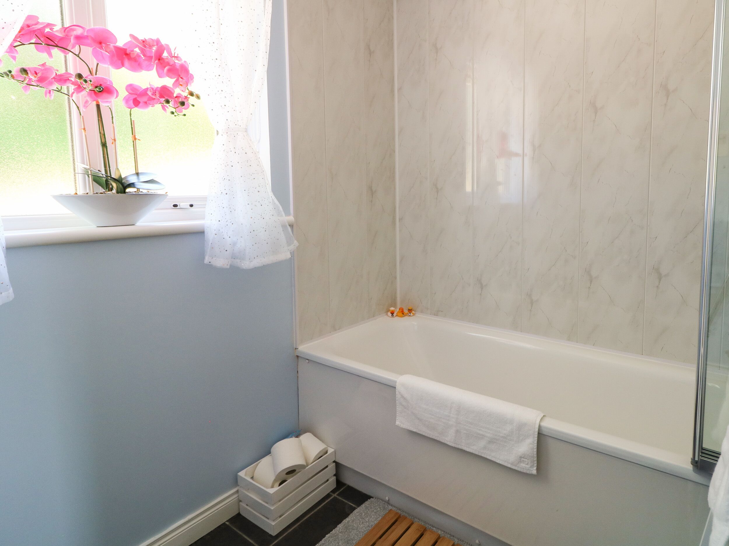 Ein Badezimmer mit einer Badewanne, einem Fenster mit einer Pflanze und einer kleinen weißen Mülltonne.
