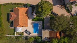 An aerial view of a house with a swimming pool, a patio with chairs, and a satellite dish.