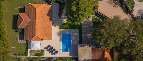 An aerial view of a house with a swimming pool, a patio with chairs, and a satellite dish.