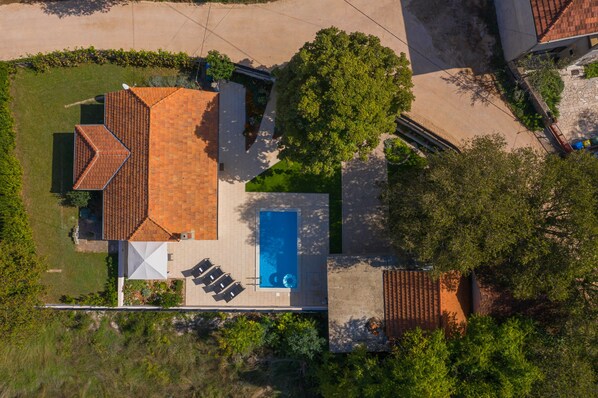 Ovenudblik over et hus med swimmingpool, terrasse med stole og en parabol.