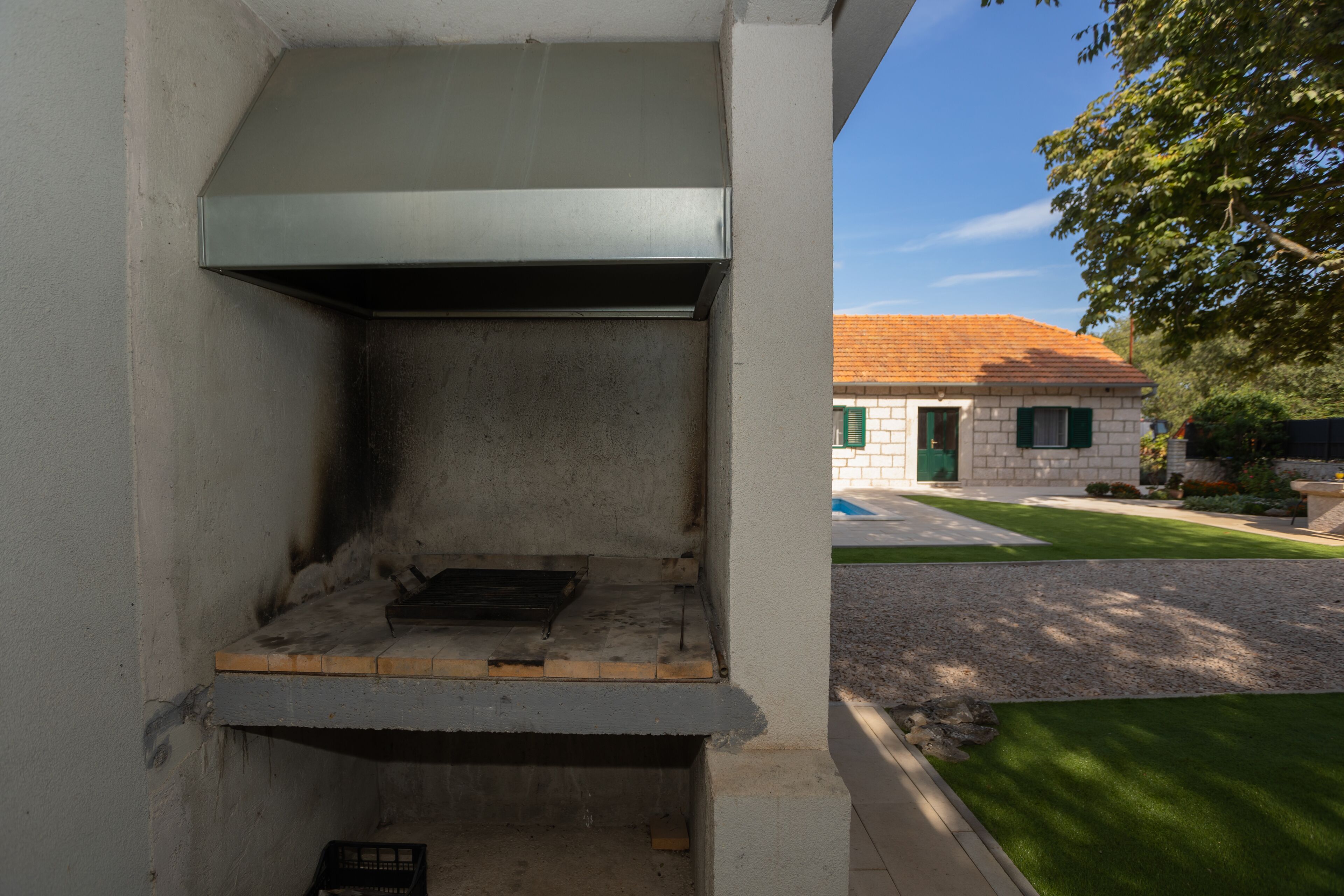 Uma área de churrasco ao ar livre com base de concreto, uma tampa de metal e uma parede de tijolos.