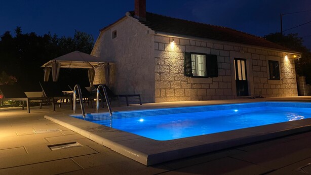 A stone building with a swimming pool, outdoor seating, and a covered area.