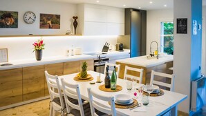 Een moderne keuken met witte kasten, een centraal eiland en een eetgedeelte met witte stoelen en een tafel voor twee.