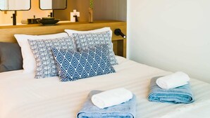 Een hotelkamer met een bed, kussens, een nachtkastje, een spiegel, een plafondventilator en een schilderij aan de muur.