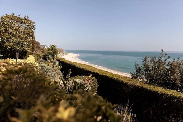 A coastal landscape with a beach, vegetation, and a clear sky.