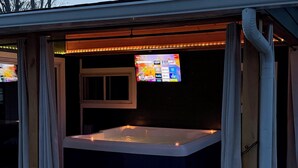 Un bain à remous doté d’un téléviseur à écran plat placé au-dessus, le tout entouré de rideaux.