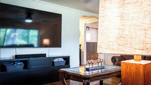 Un salon avec un téléviseur à écran plat fixé au mur, une table basse en bois et une lampe.