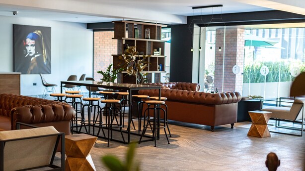 Una sala de estar moderna con un sofá de cuero marrón, una zona de comedor con taburetes de bar y una estantería.
