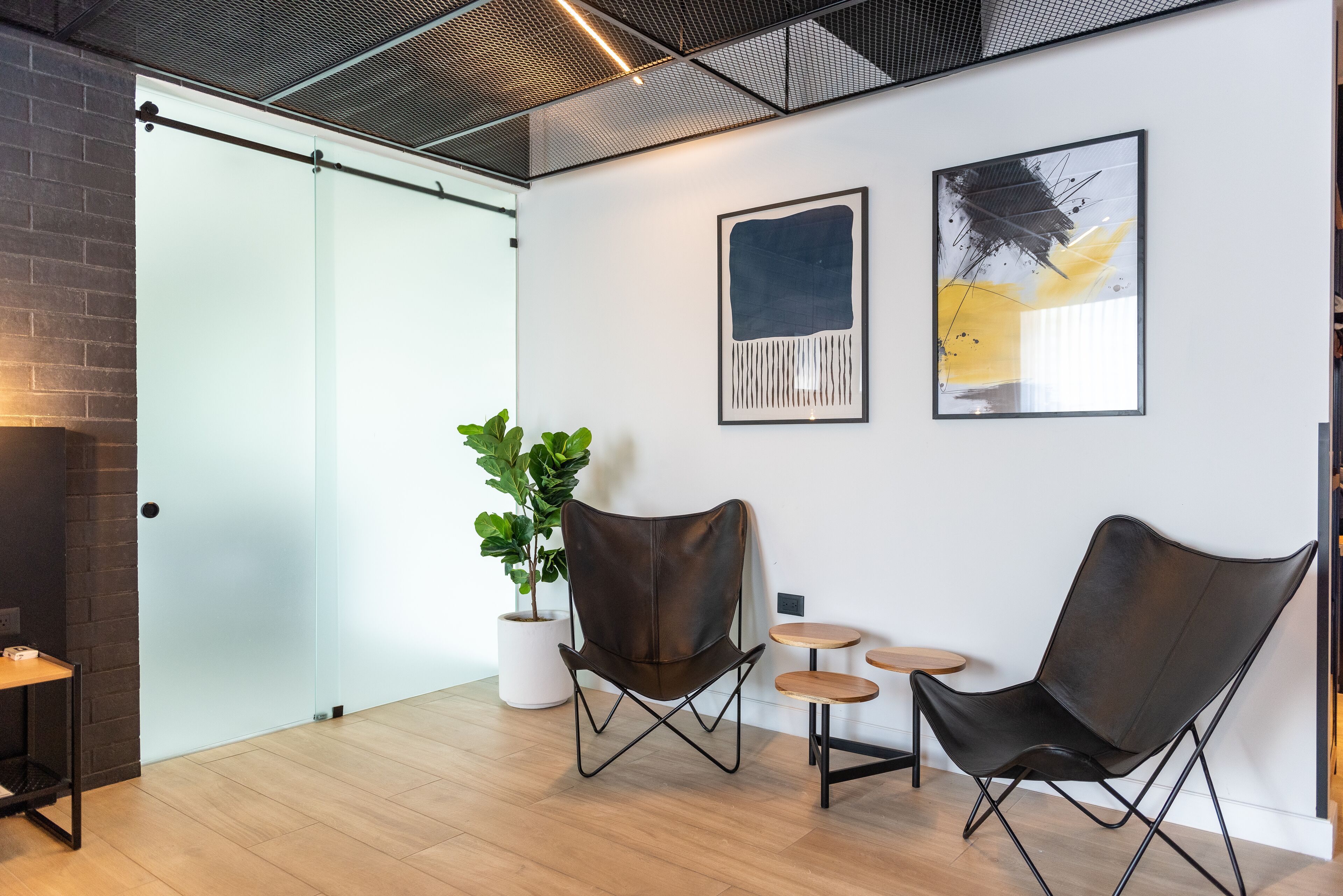 A modern office space with two leather chairs, a small wooden table, and a potted plant.