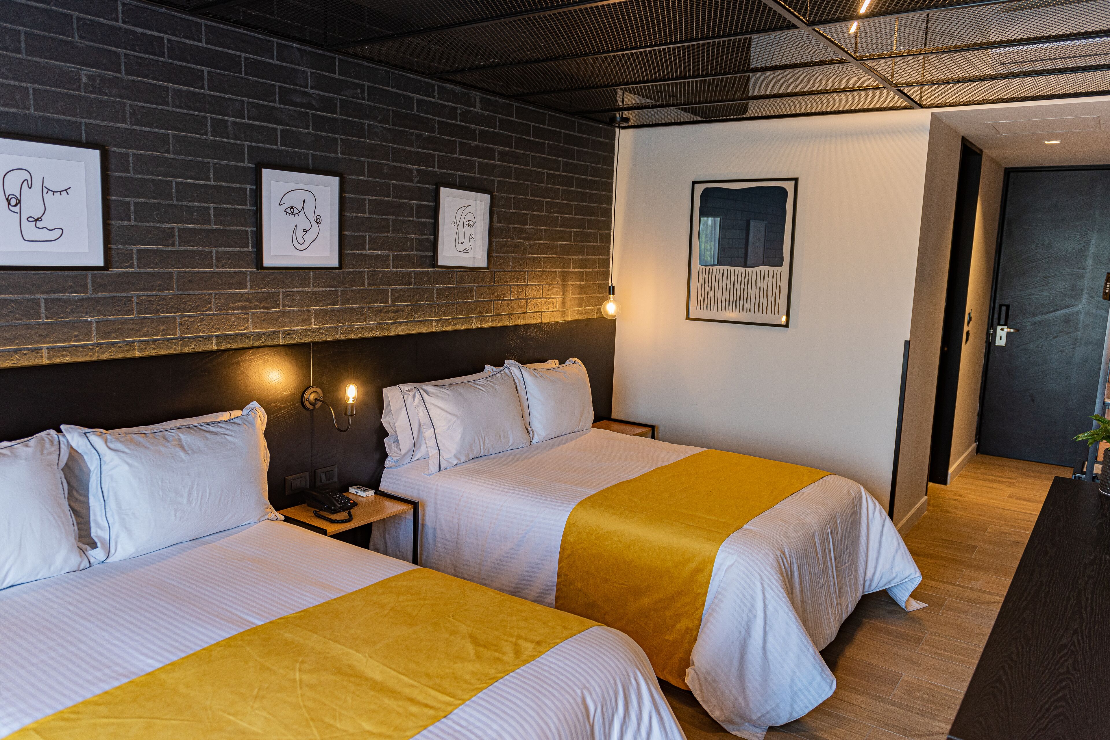 A hotel room with two beds, a brick wall, and artwork.