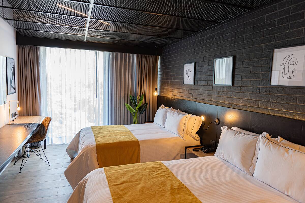 Habitació d'hotel amb dos llits, escriptori i una finestra gran amb cortines.