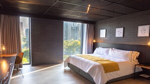 Un dormitorio moderno con una cama grande, un escritorio y vistas a la ciudad a través de un amplio ventanal.