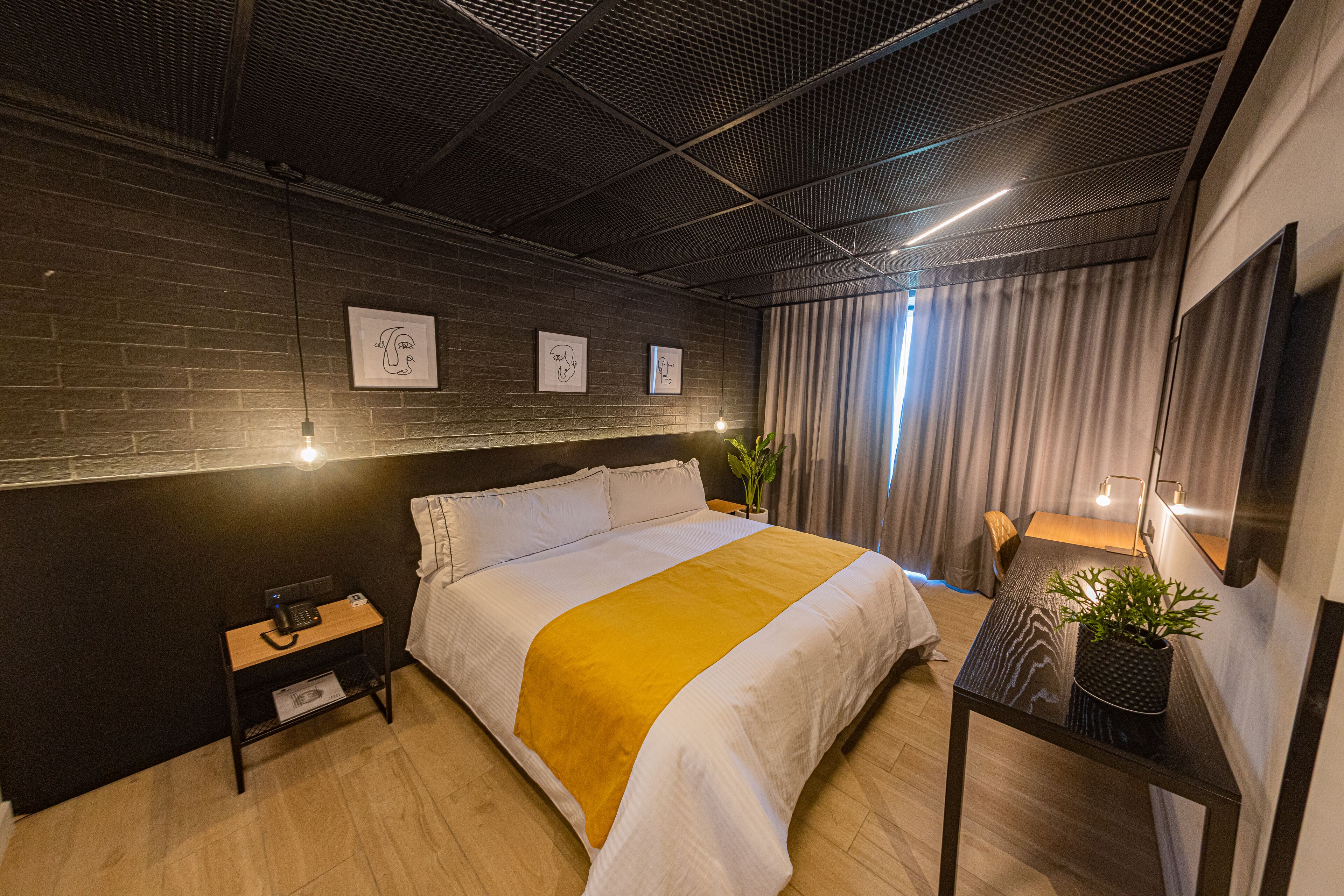 A modern hotel room with a large bed, a small table with a plant, and artwork on the wall.