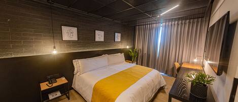 A modern hotel room with a large bed, a small table with a plant, and artwork on the wall.