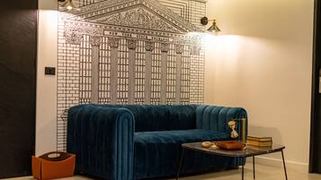 A room with a blue velvet sofa, a small table with books and a lamp, and a wall mural of the New York Stock Exchange.