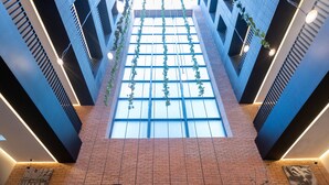 Zona de recepción de hotel con pared de ladrillo, mostrador de recepción y un gran ventanal que permite la entrada de luz natural.