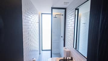 Un baño moderno con paredes de ladrillo blanco, un espejo grande, un lavamanos blanco y un inodoro.