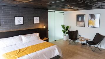 A modern hotel room with a large bed, a small desk, a potted plant, and two chairs.
