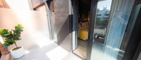 A modern interior with a bed, a potted plant, and a sliding glass door leading to a balcony.