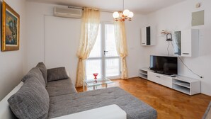 A modern living room with a grey sofa, a glass coffee table, a flat-screen TV, and a white entertainment unit. - A1 - apt w. the sea View, two Terraces and Garden (Kastela)