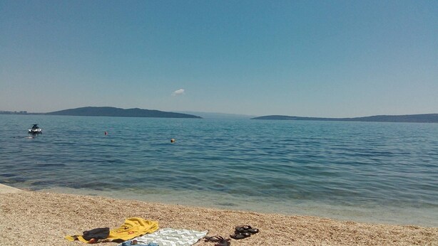 A beach with a pebbly shore, a jet ski in the water, and distant hills. - A1 - apt w. the sea View, two Terraces and Garden (Kastela)