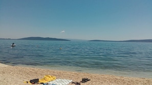 Une plage au rivage de galets, un jet-ski sur l’eau et des collines à l’horizon.