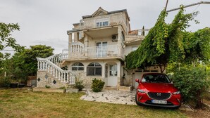 A two-story house with a stone facade, a white balcony, and a red car parked in front. - A1 - apt w. the sea View, two Terraces and Garden (Kastela)