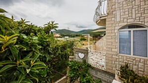 A stone building with a balcony, surrounded by lush greenery and a mountainous backdrop. - A1 - apt w. the sea View, two Terraces and Garden (Kastela)
