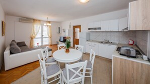A modern kitchen with white cabinets, a dining area with a round table and chairs, and a living area with a sofa and a TV. - A1 - apt w. the sea View, two Terraces and Garden (Kastela)