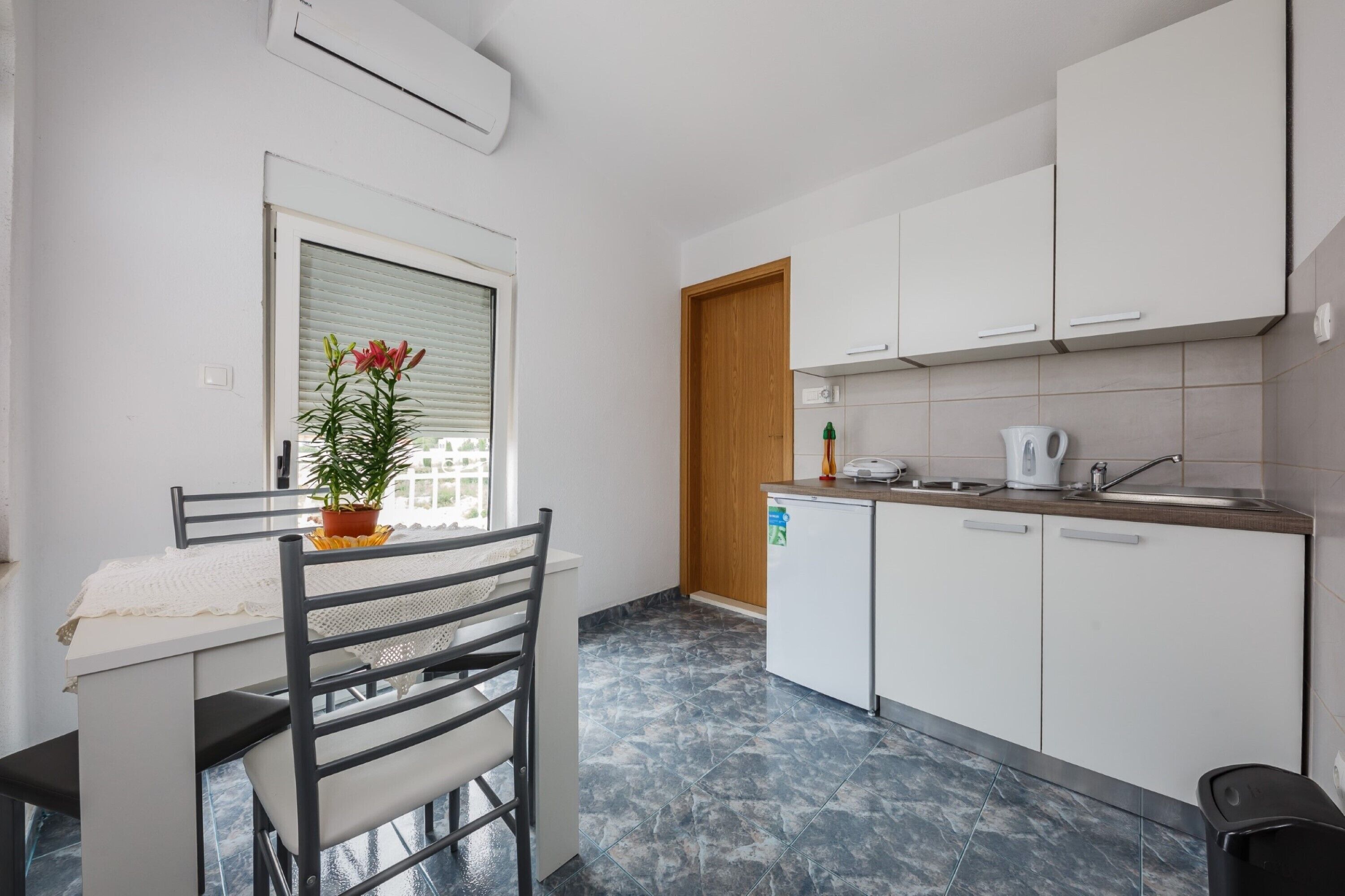 A compact kitchen with white cabinets, a small countertop, and a window with a potted plant.
