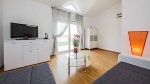 Ein modernes Wohnzimmer mit Fernseher, einem Glastisch mit Topfpflanze und einer Couch.
