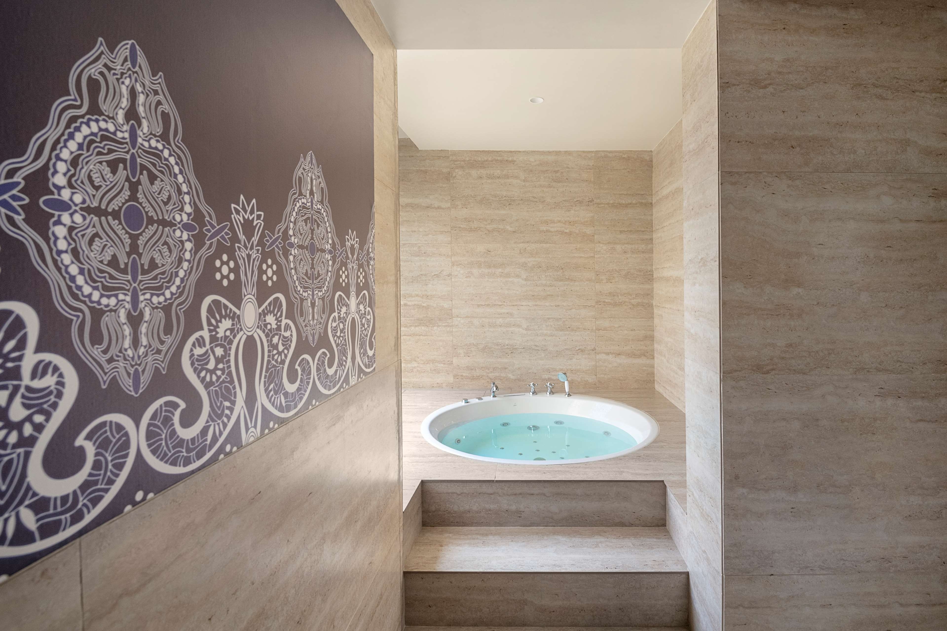 A modern bathroom with a freestanding bathtub, a wooden floor, and a decorative wall with intricate patterns.