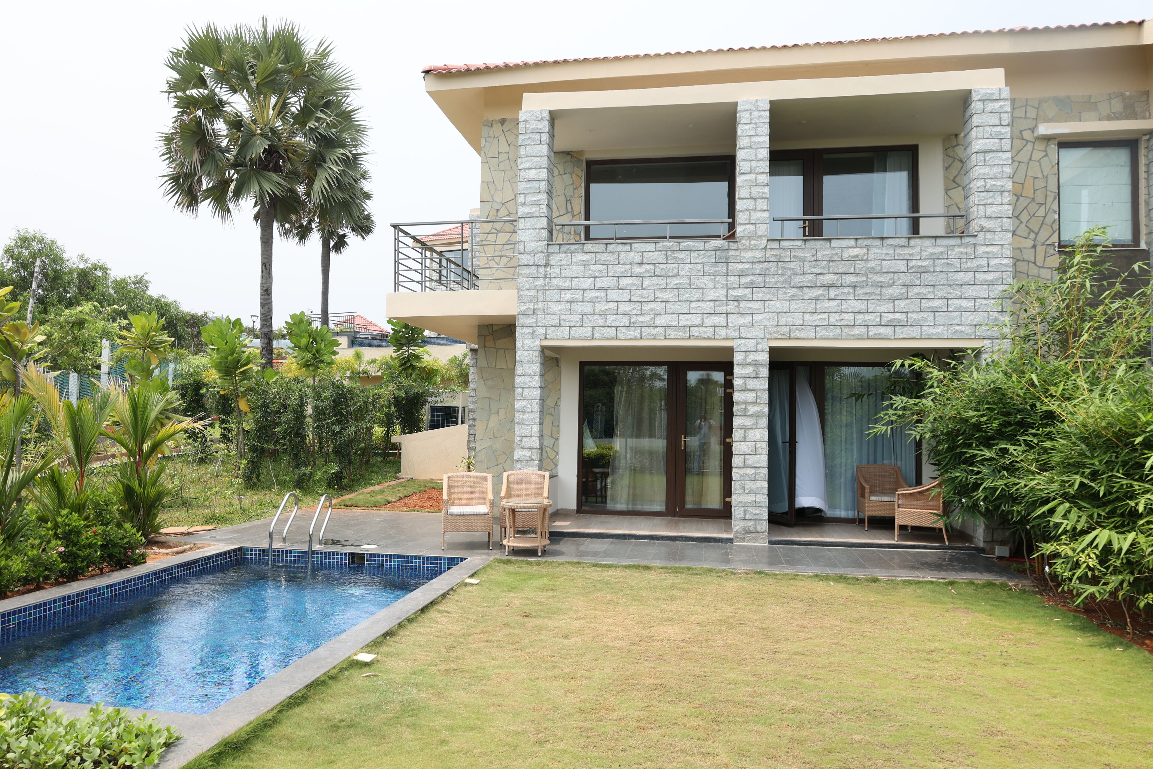 A modern two-story house with a swimming pool, outdoor seating, and lush greenery.