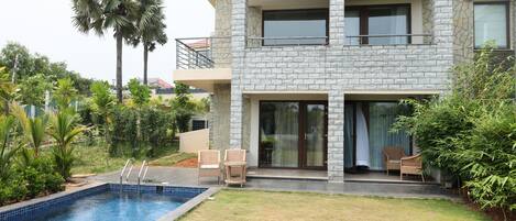 A modern two-story house with a swimming pool, outdoor seating, and lush greenery.