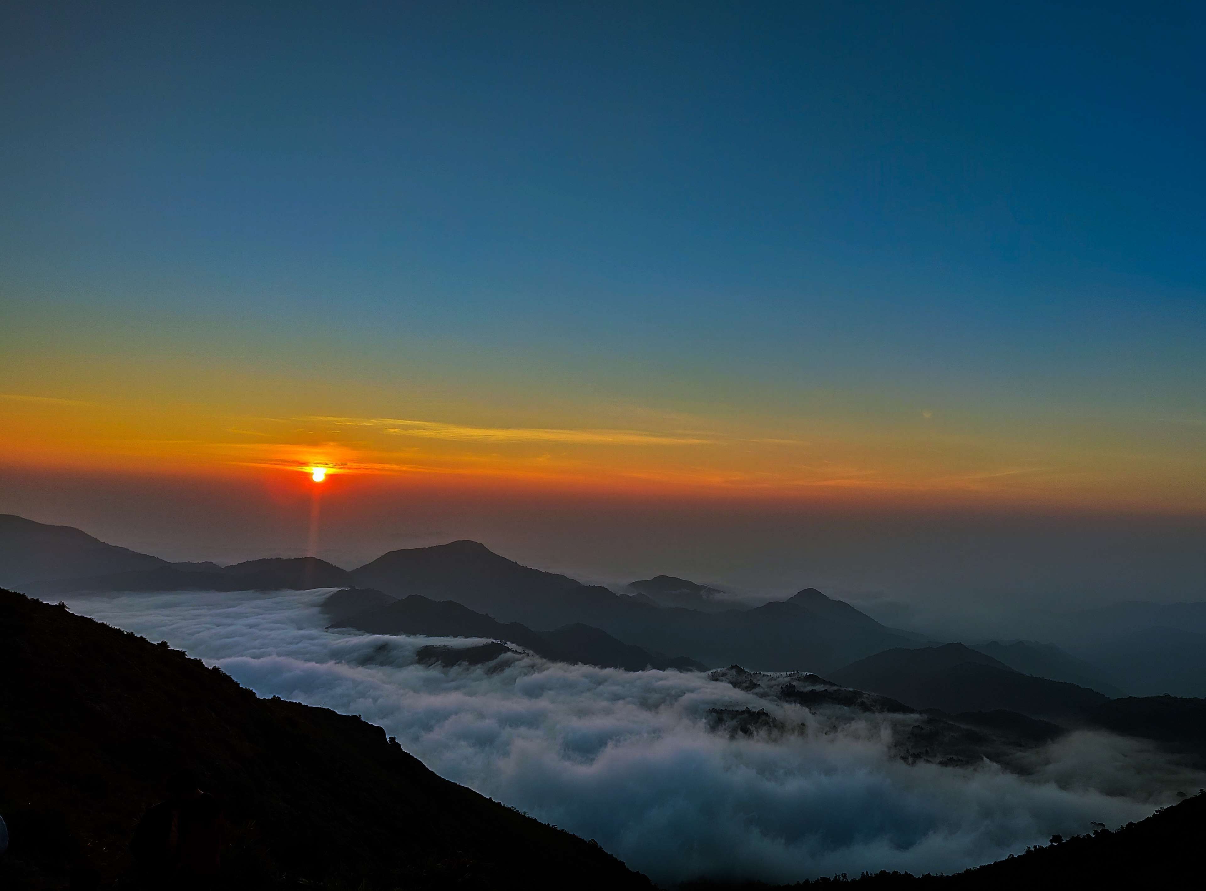 A mountain landscape at sunrise with clouds below the peaks.