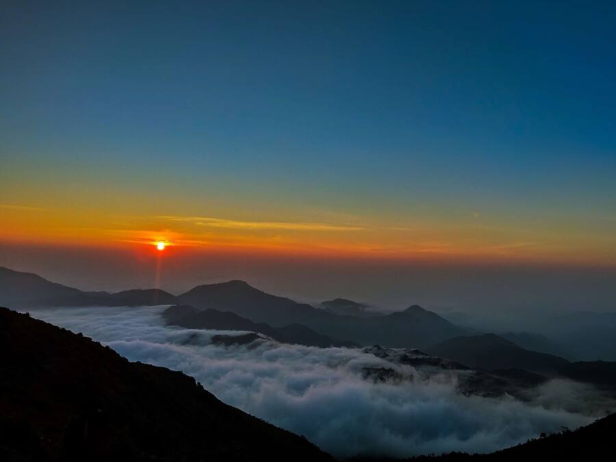 A mountain landscape at sunrise with clouds below the peaks.